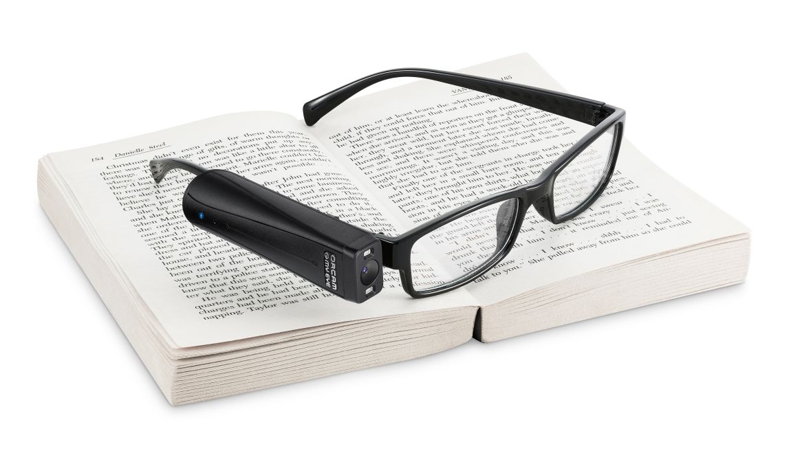 Das Bild zeigt die OrCam Brillenkamera auf einem Buch liegend.